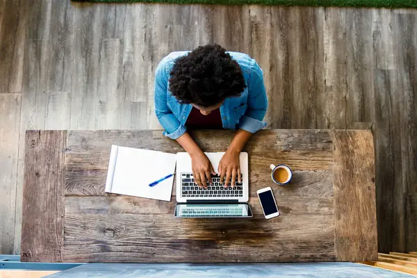 An overhead view of someone writing at a wooden desk